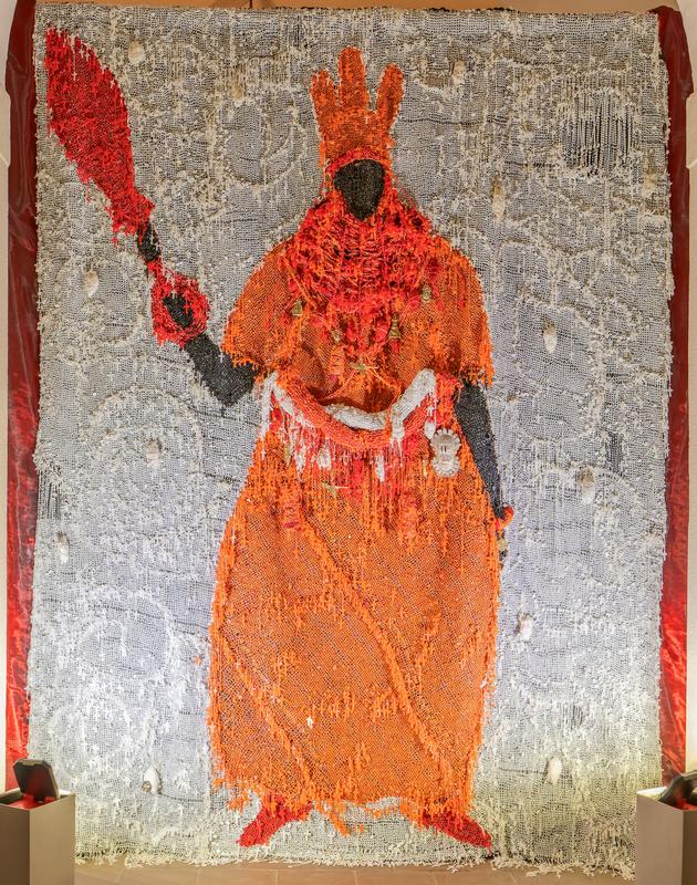Multimedia woven hanging, depicting a standing Black figure wearing a crown and an orange robe with an ornate belt and holding a spear