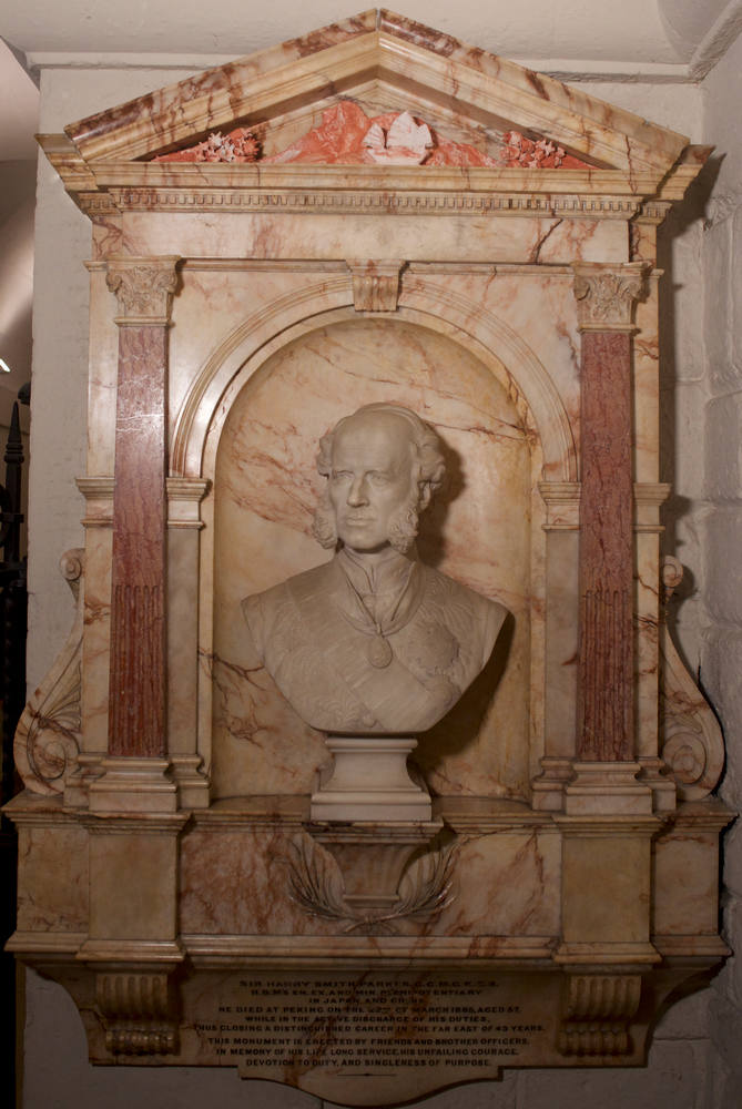 marble portrait bust of a man with a bald pate and impressive sideburns, set into a marble alcove - in the pediment, an orange clay outline of a mountain with a small, white clay sampan sailing in front