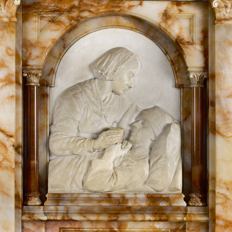 Close-up of Whire marble relief showing a woman in profile lifting the head of a bed-ridden man and giving him a drink from a glass, set into an ornate surround sculpted from a marble with distinct orangey-brown markings