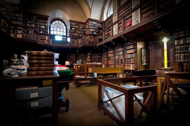 An old library lined with books on dark wooden shelves and with a wooden walkway running round half way up