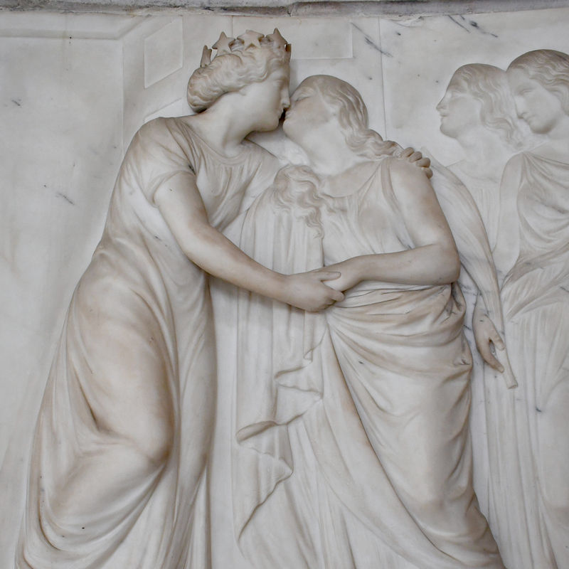 marble relief showing two robed women embracing and giving and receiving a kiss