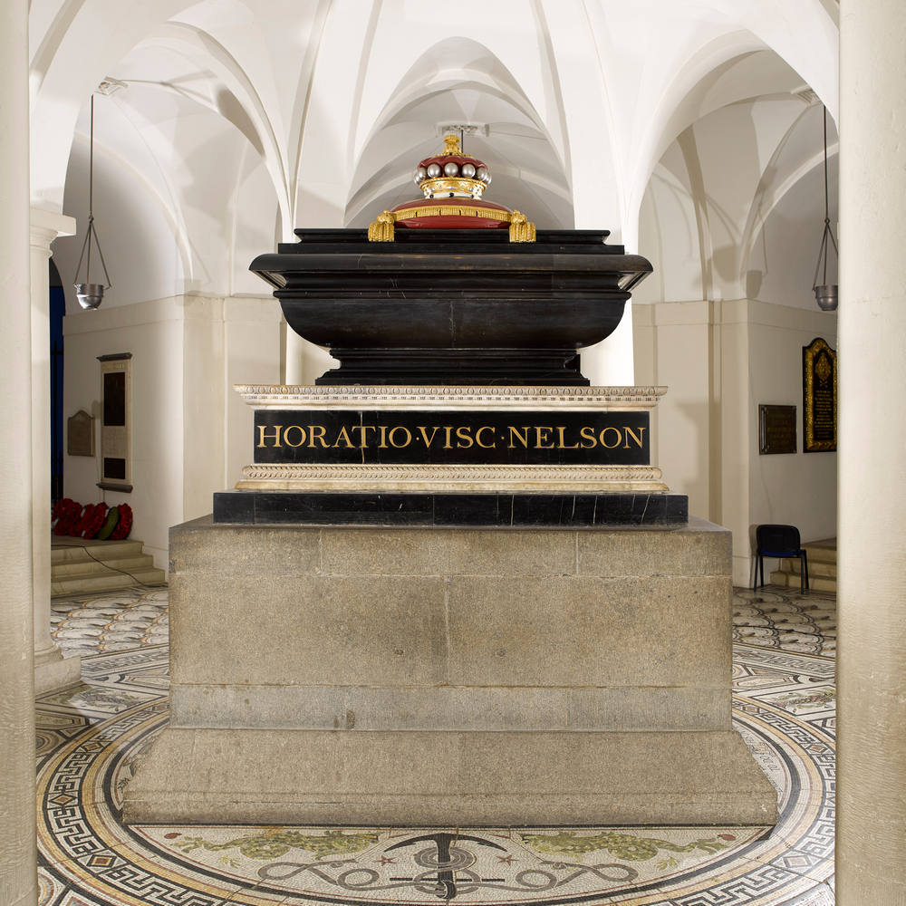 Black marble sarcophagus topped with a gold and red crown, on a massive stone plinth
