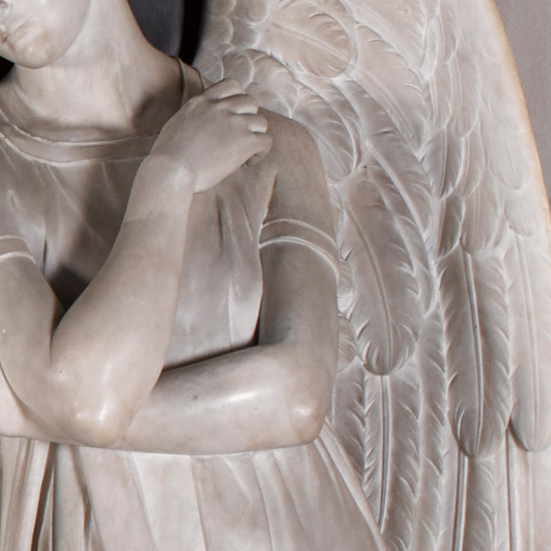 close up of marble angel showing arms bent across his/her body and One feathered wing 