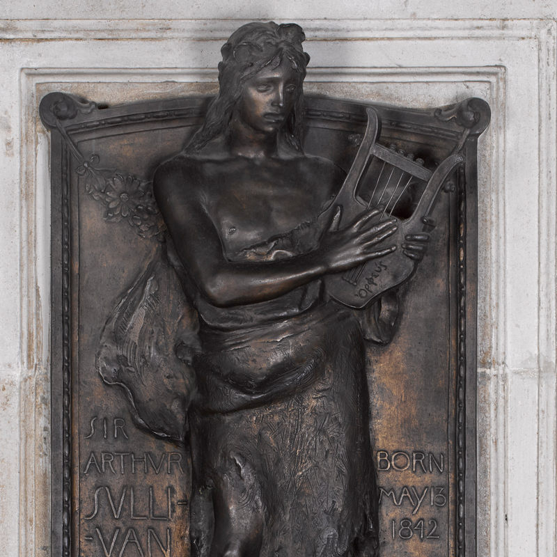 Bronze wall panel showing bare-chested man playing a lyre