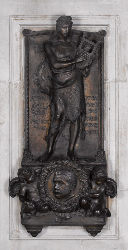 Bronze wall panel showing bare-chested man playing a lyre, set over a roundel portrait head of man with a moustache