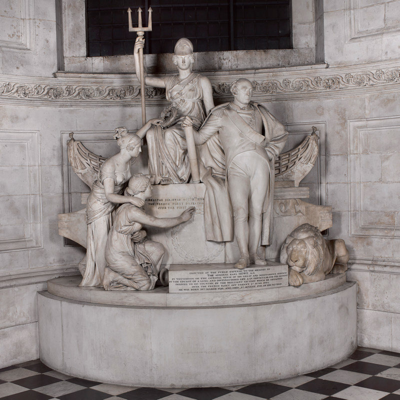 Large marble monument with life-sized admiral a tthe centre, Britannia with a trident behind, and other allegorical figures pointing to the inscription on a tomb.