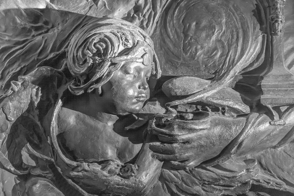 Close-up of bronze cherub, blowing smoke from a lamp or incense burner, under an over-exposing white light