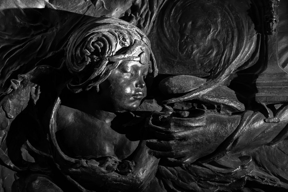 Close-up of bronze cherub, blowing smoke from a lamp or incense burner, black under a white light.