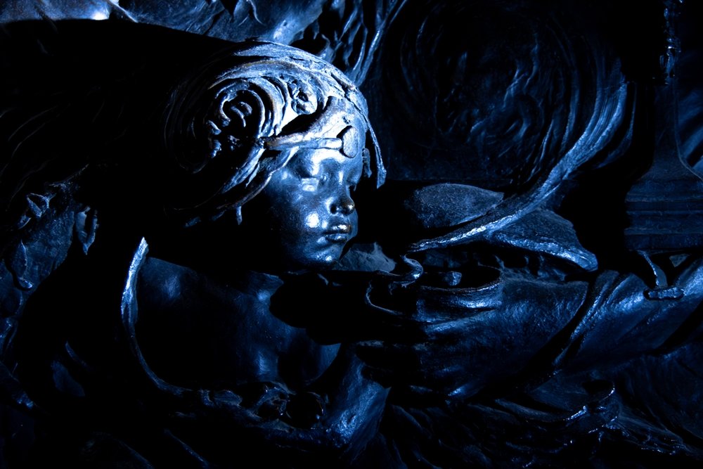 Close-up of bronze cherub, blowing smoke from a lamp or incense burner, darkened.