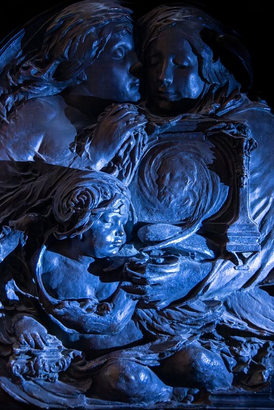 Bronze relief panel with three figures, in a blueish light