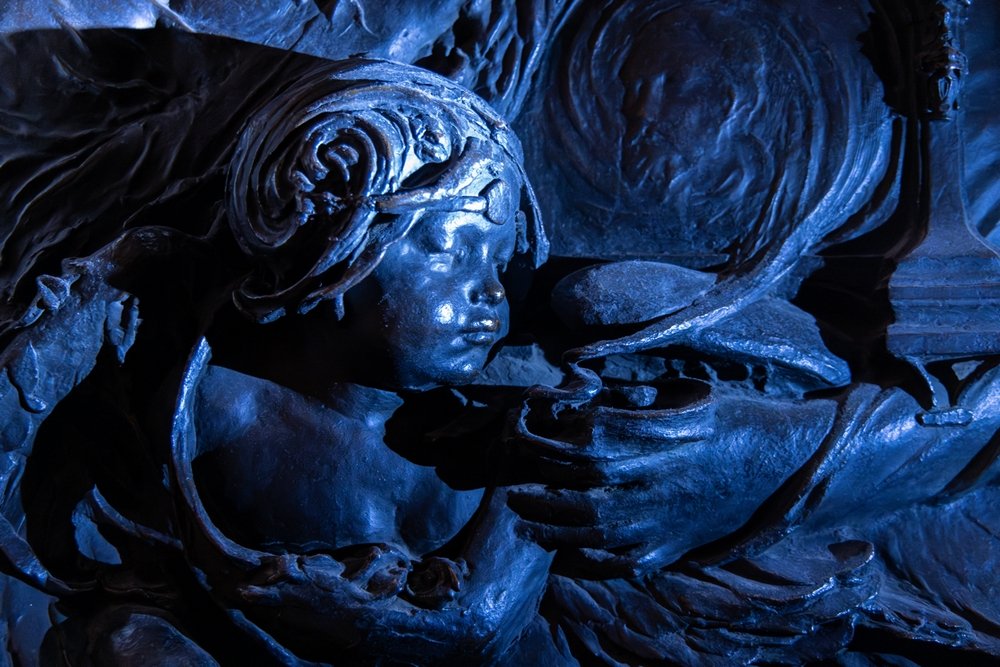 Close-up of bronze cherub, blowing smoke from a lamp or incense burner, in a blueish light.