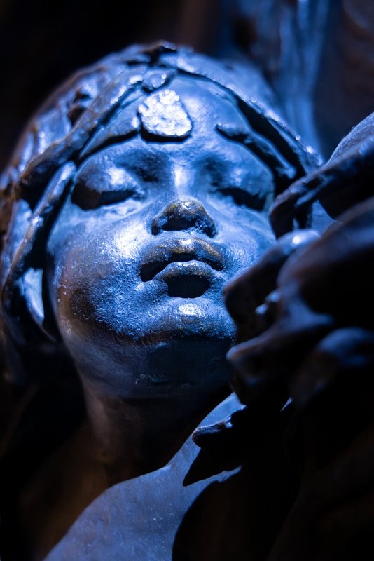 Close-up of bronze cherub's face, in a blueish light