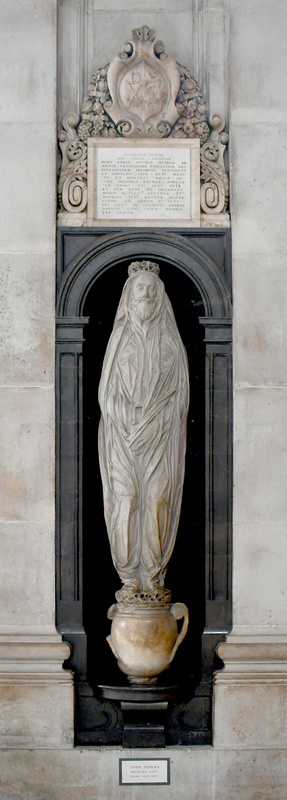 White marble sculpture of a bearded man wearing a shroud, standing on an urn, set into a black marble surround.