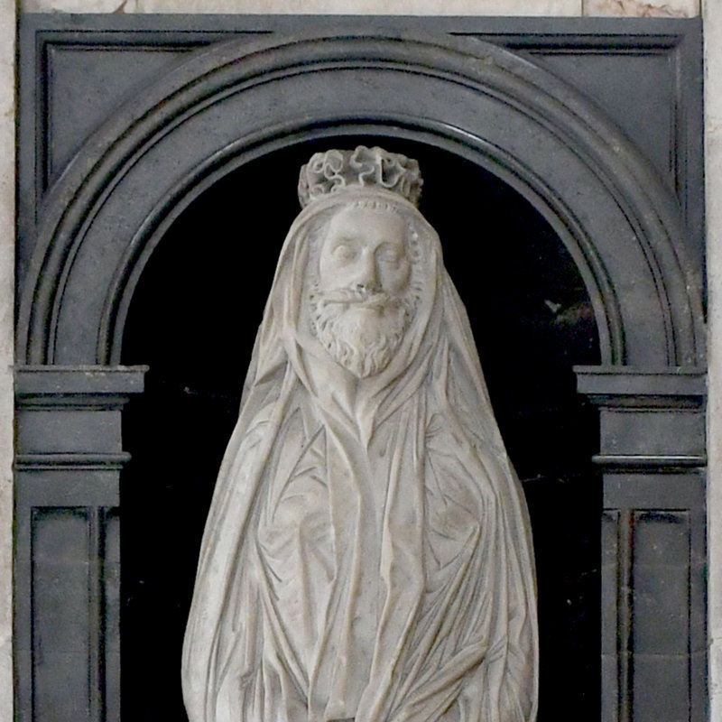 Detail of a white marble sculpture of a bearded man wearing a shroud, set into a black marble surround.